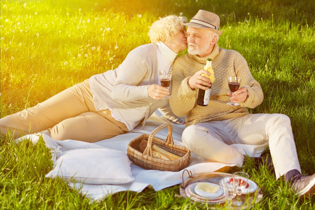 älteres Pärchen picknickt im Gras bei Sonnenschein