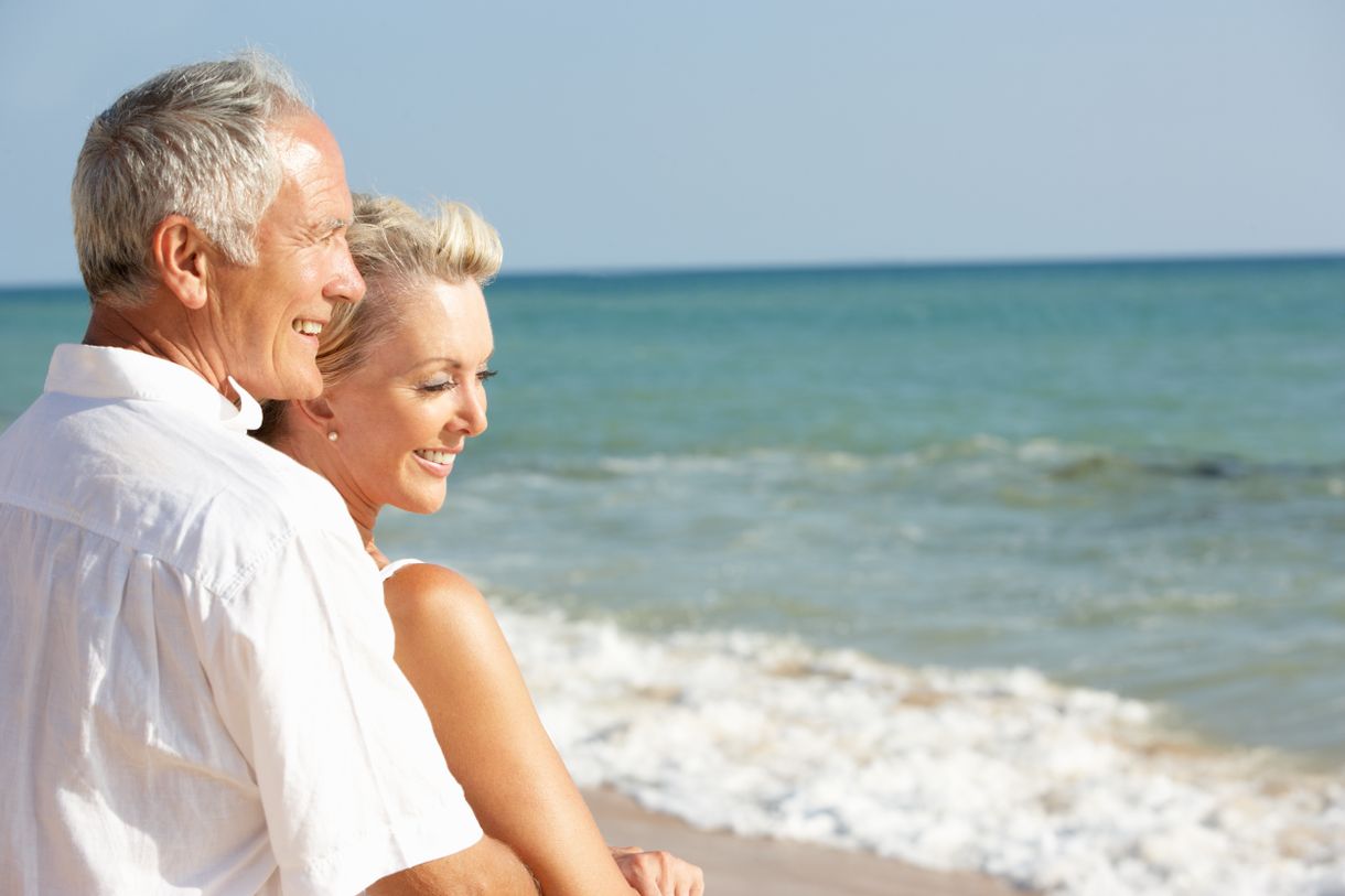 älterer Mann umarmt Frau von hinten am Strand, blicken auf das Meer