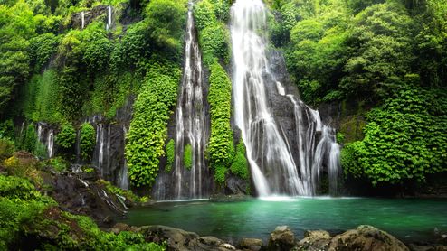 Ein Wasserfall fällt in ein Becken mit türkisblauem Wasser.