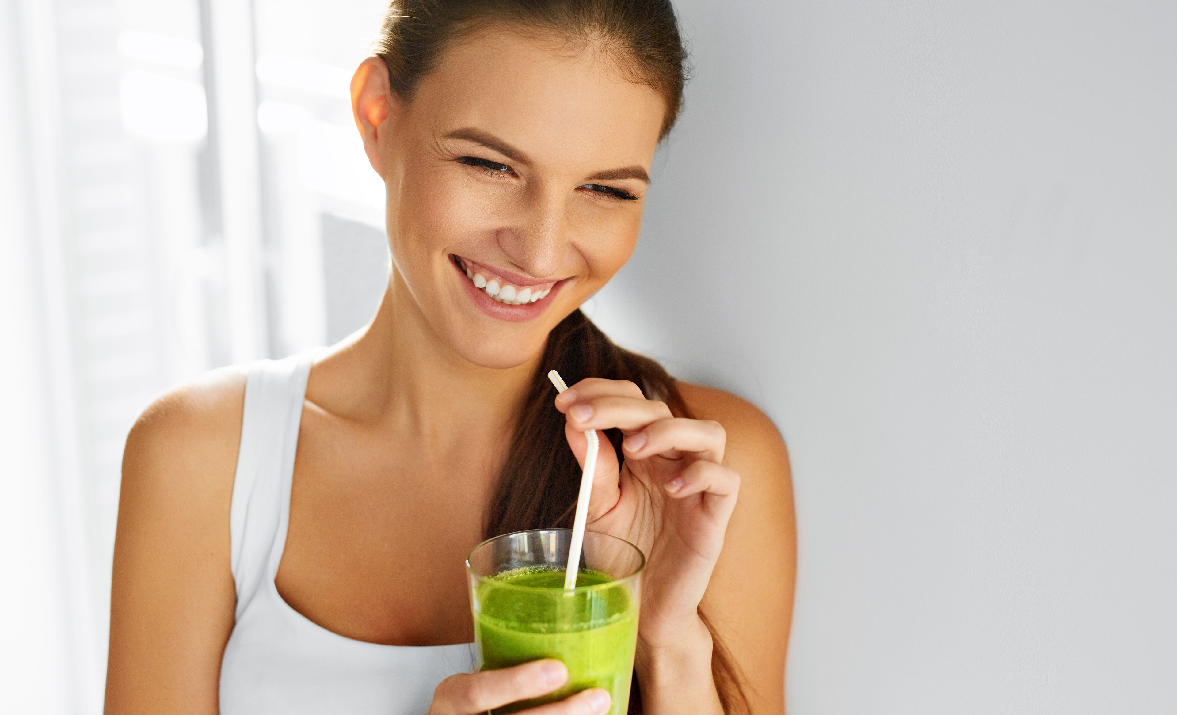 Eine lächelnde Frau mit einem grünen Smoothie in den Händen