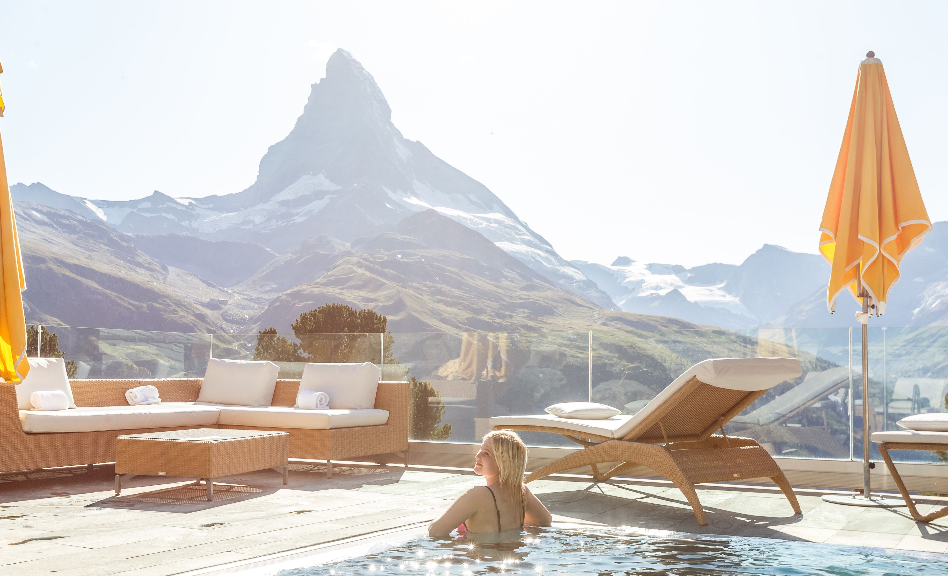 Frau im Pool einer Hotelterrasse mit Ausblick auf die Berge
