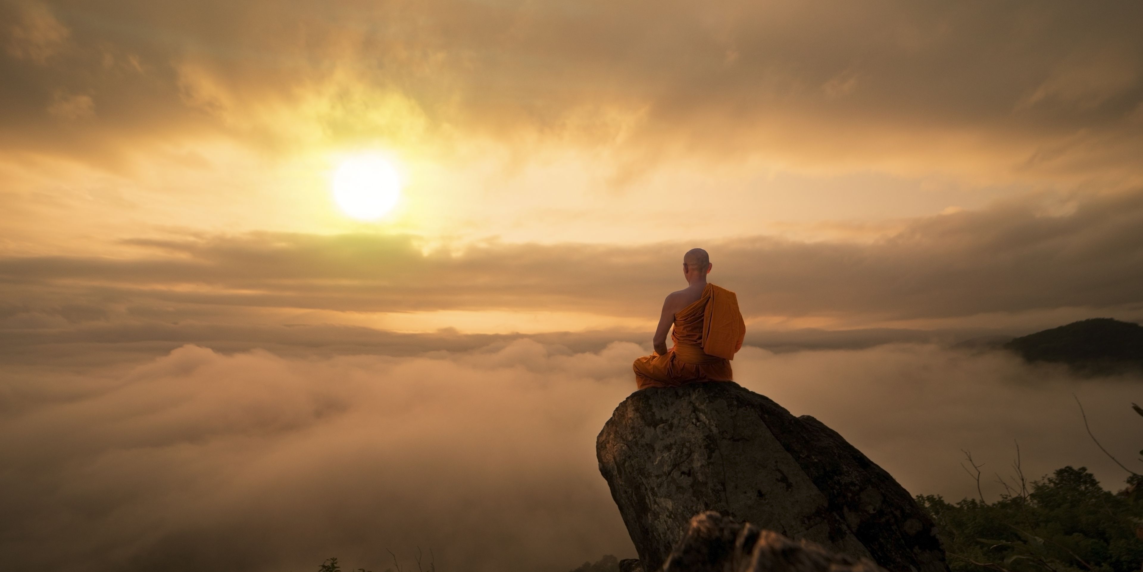 Mann auf einem Felsen sitzend mit beeindruckendem Ausblick auf eine Wolkendecke bei Sonnenaufgang