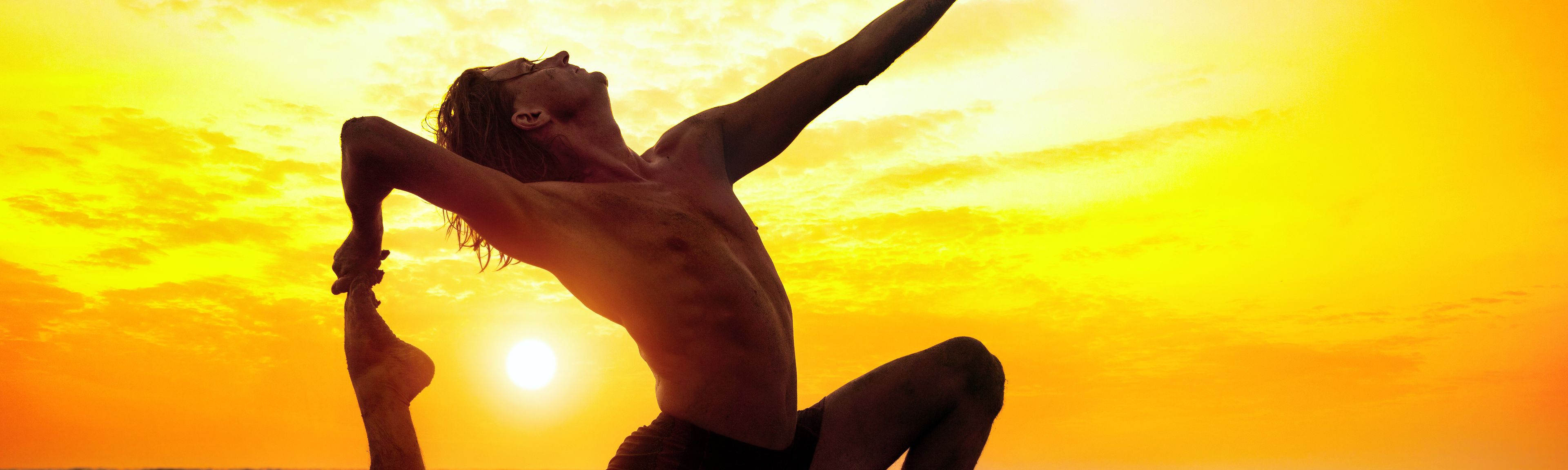 Mann in Yoga Position vor einem Sonnenuntergang am Meer
