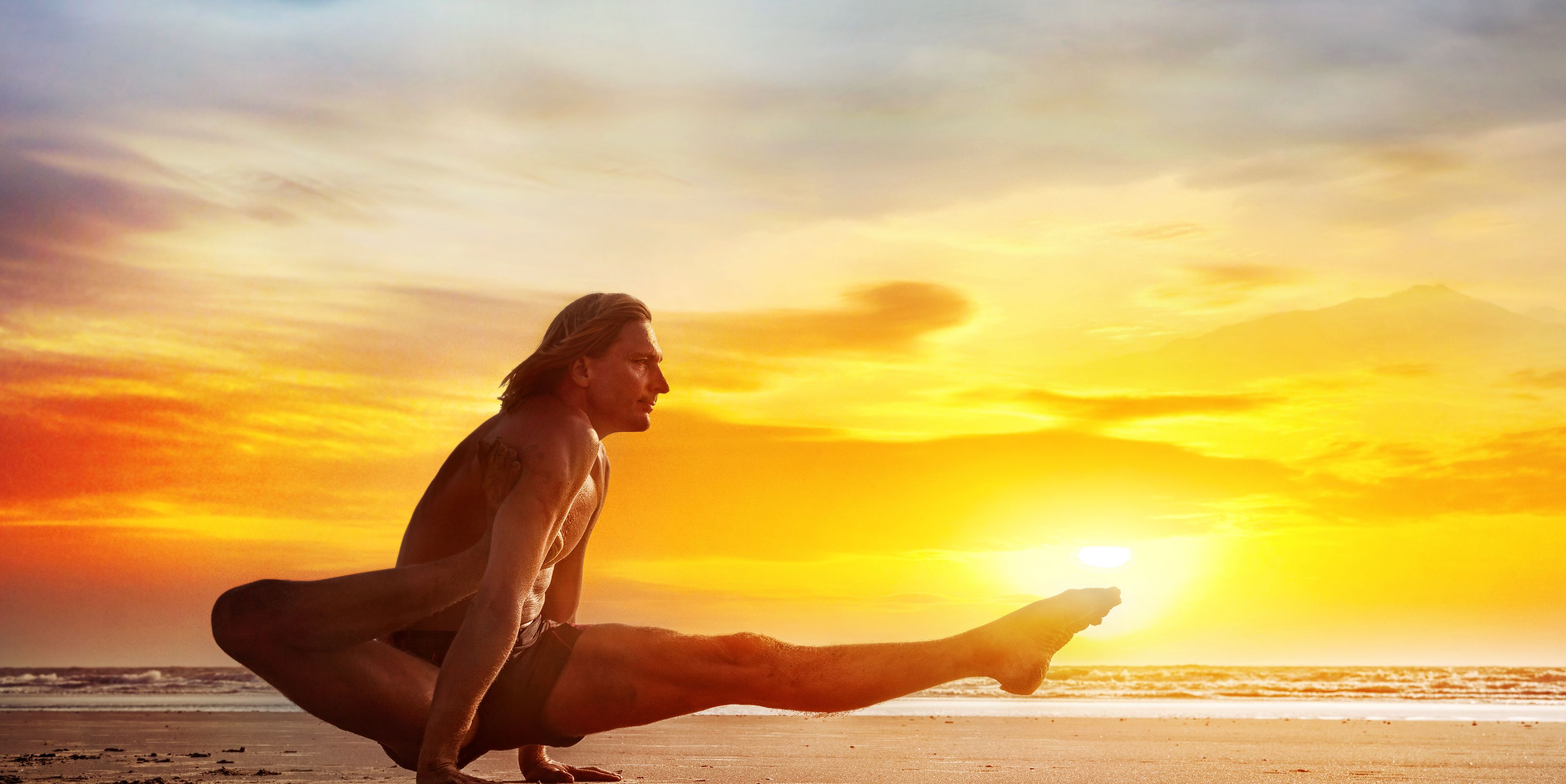 Mann in Yoga  Position vor einem Sonnenuntergang am Meer