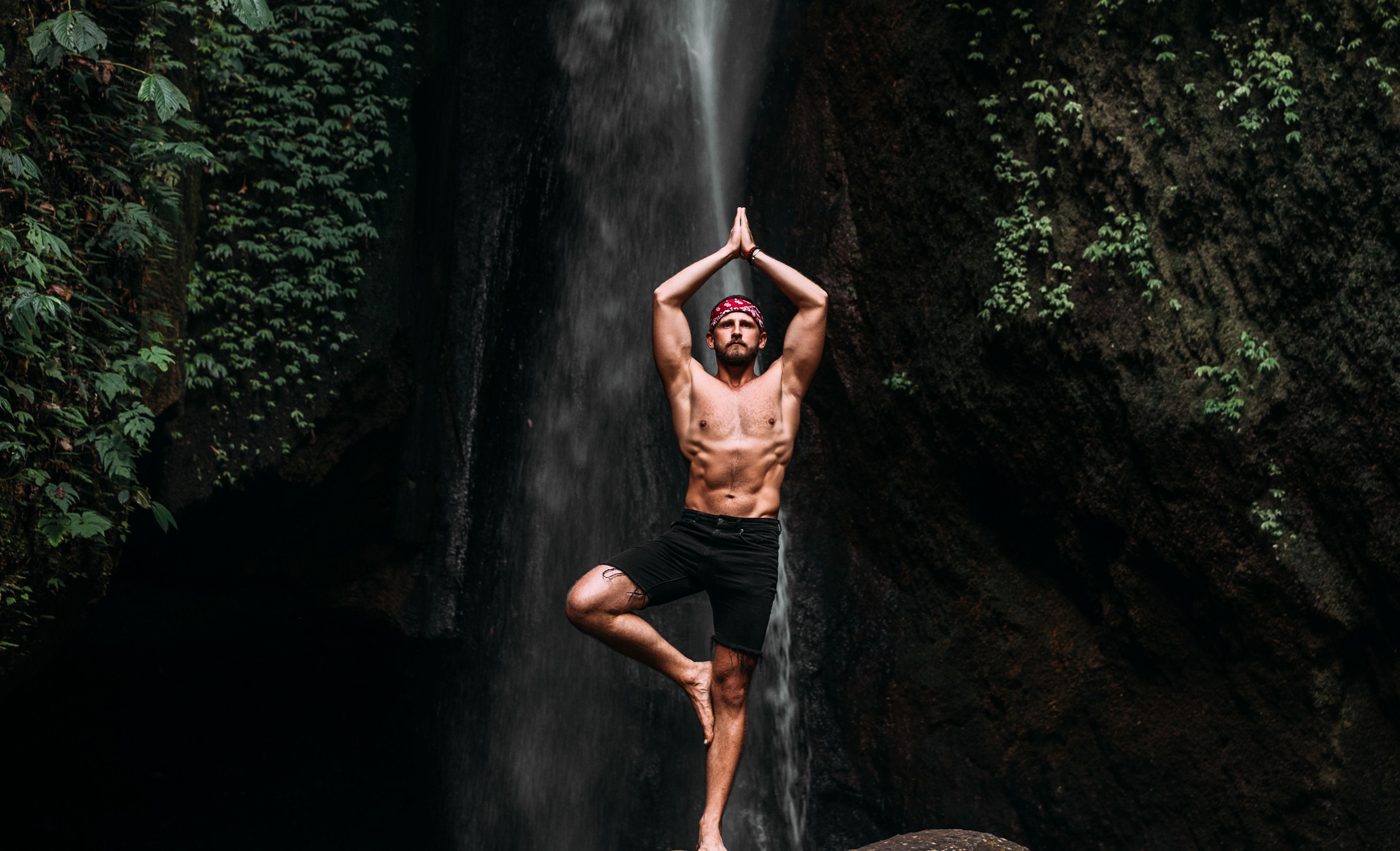 Mann in Yogastellung vor einem Wasserfall