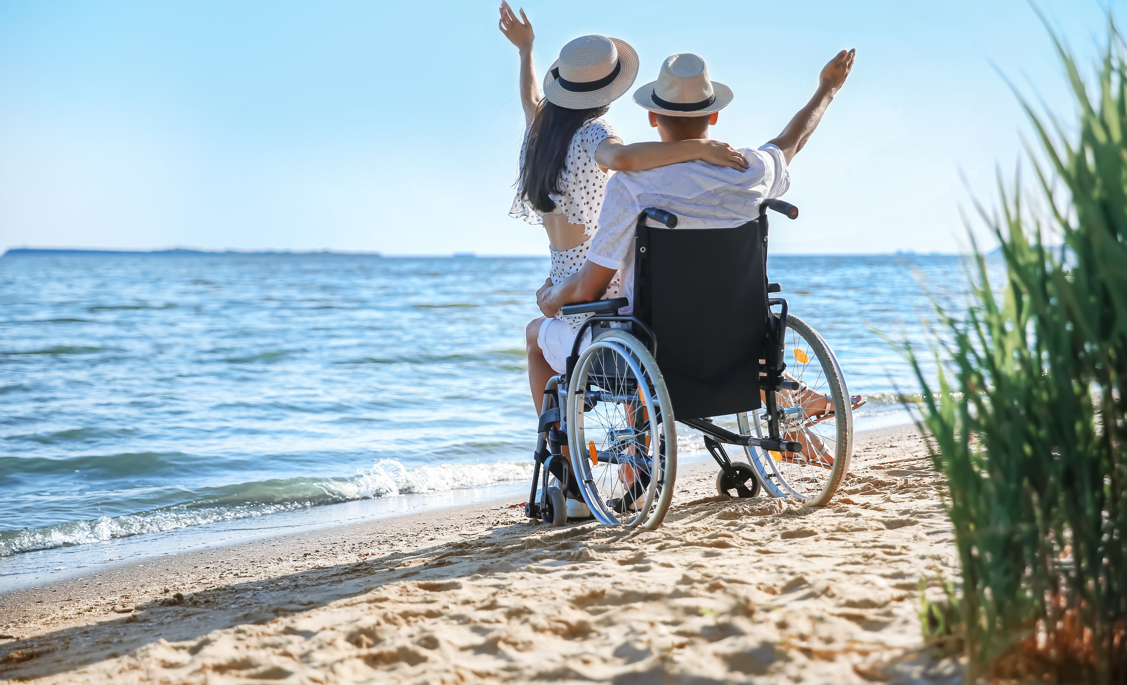Mann im Rollstuhl mit Partnerin am Strand