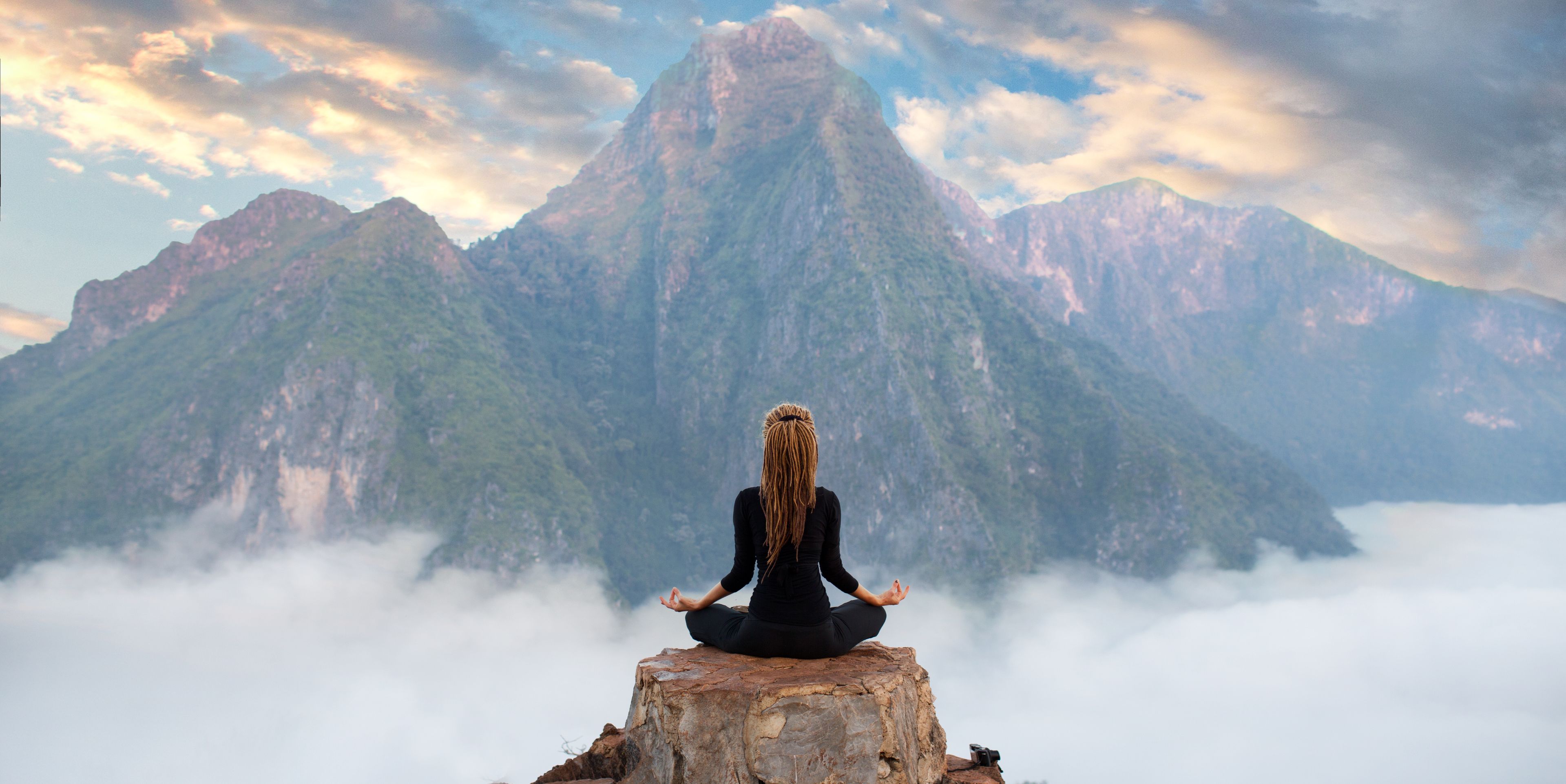 Frau im Lotussitz auf einer Bergspitze im Hintergrund eine beeindruckende Berglandschaft