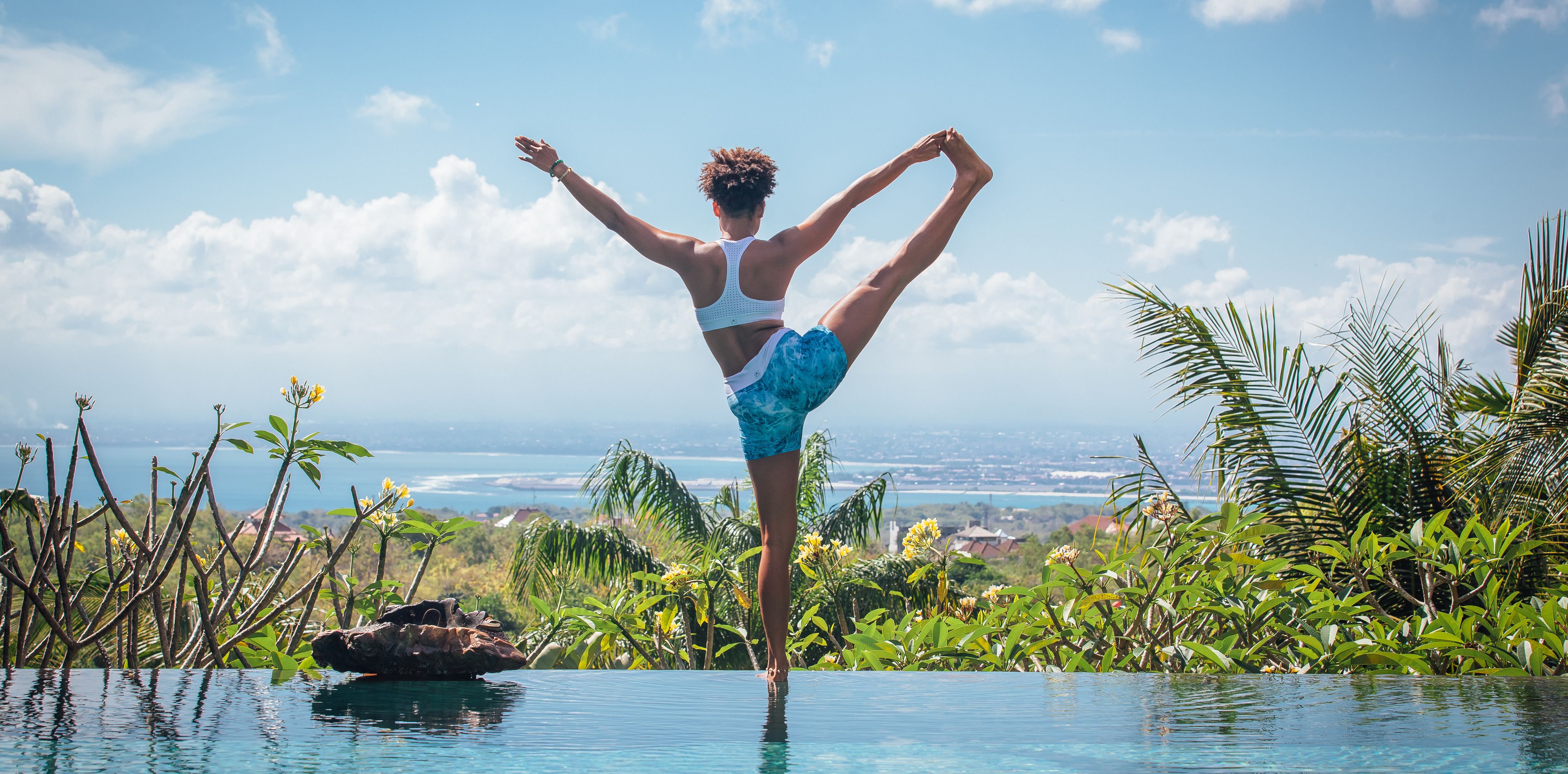 Frau in Yogastellung am Rande eines Pools mit Blick auf eine Landschaft 