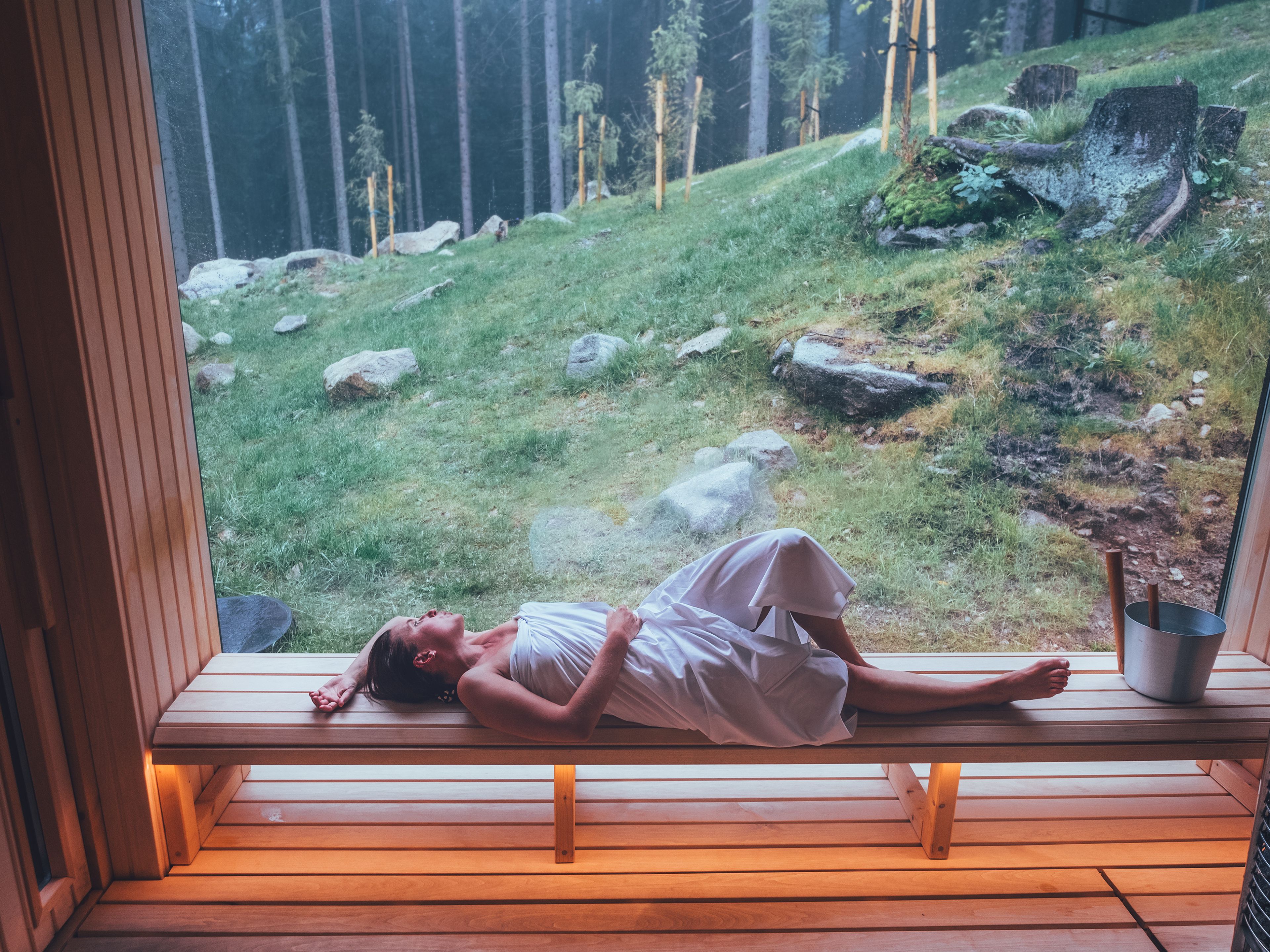 Frau entspannt in der Sauna mit Blick auf den Wald
