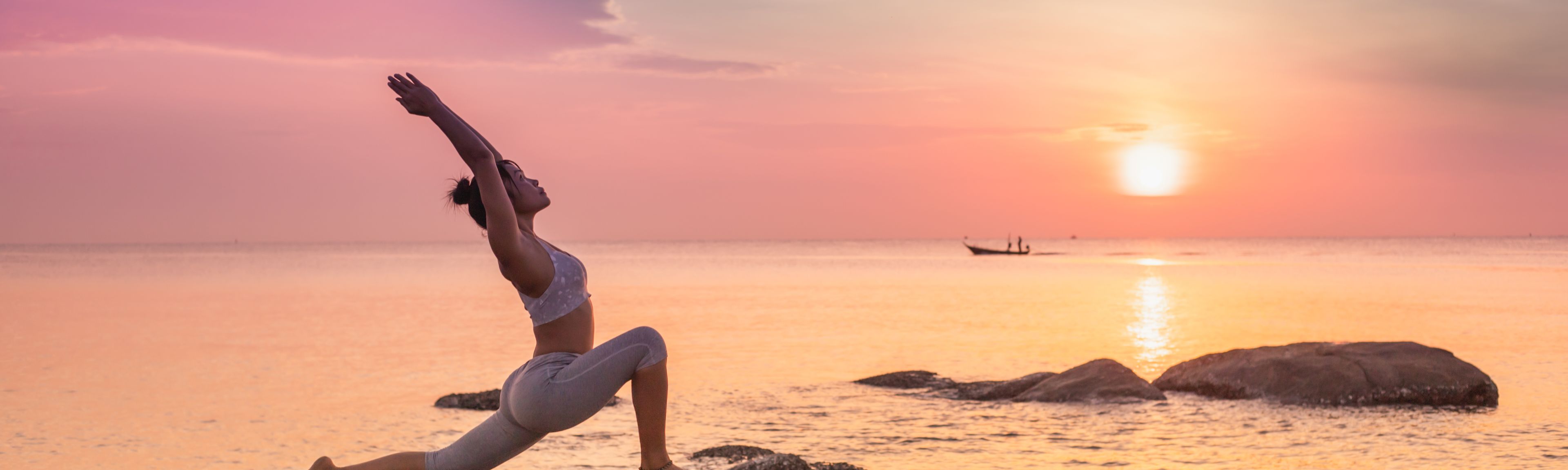 Frau in Yogastellung auf einem Felsen am Meer bei Sonnenuntergang