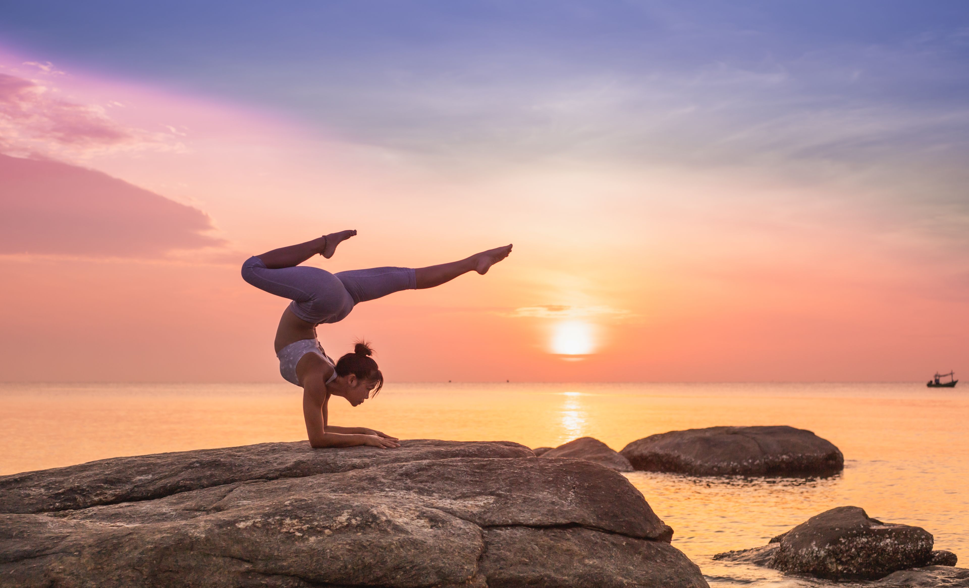 Frau in Yogapose auf einem Felsen beim Sonnenuntergang