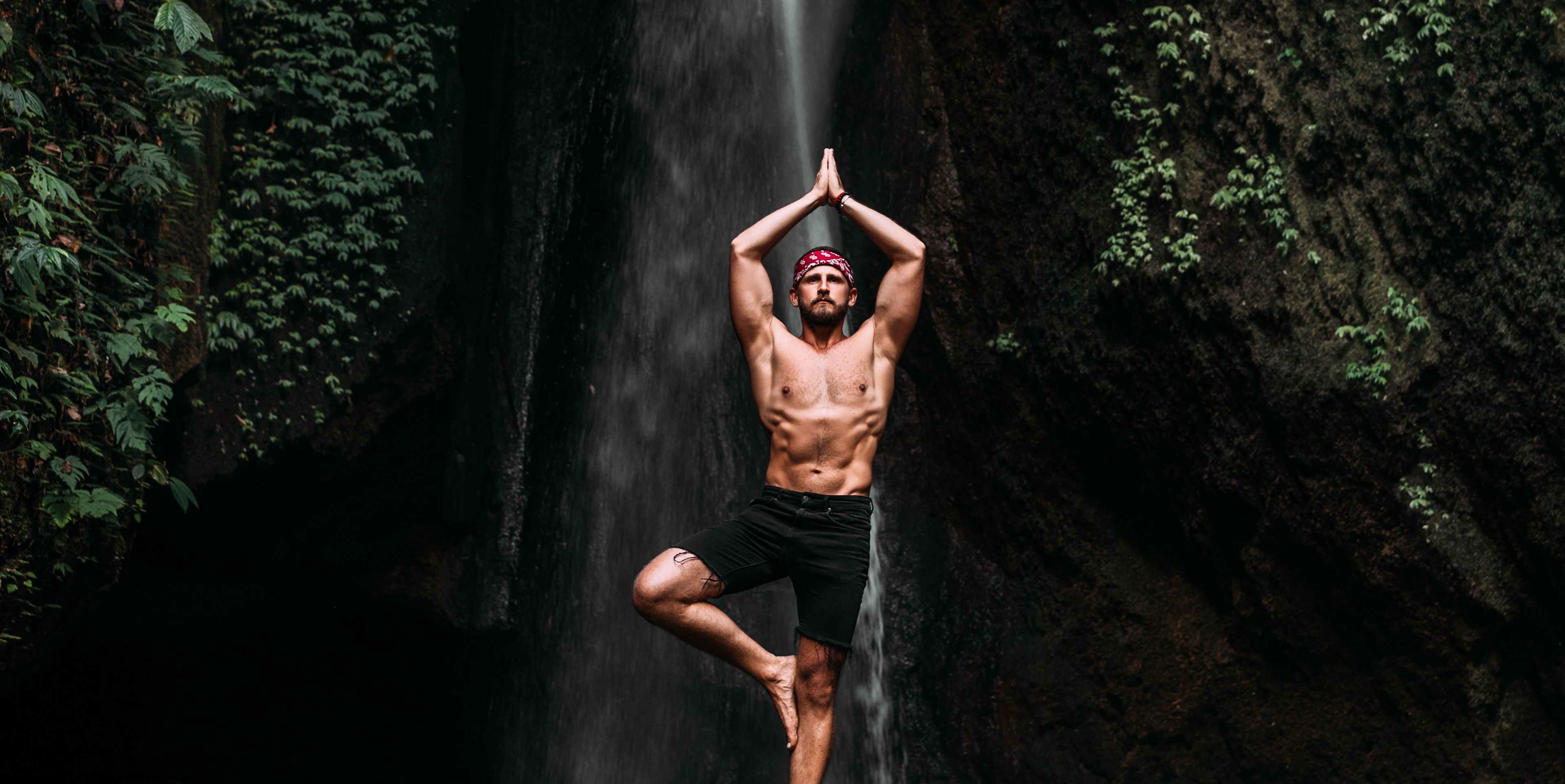 Mann in der Yoga Pose des Baumes vor einem Wasserfall