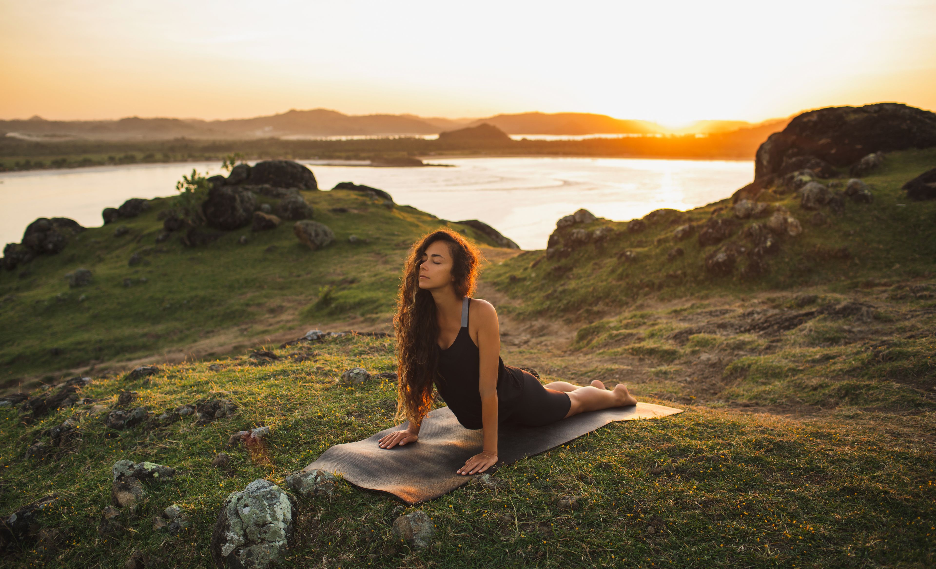 Frau in Yogaposition an einem See bei Abendlicht
