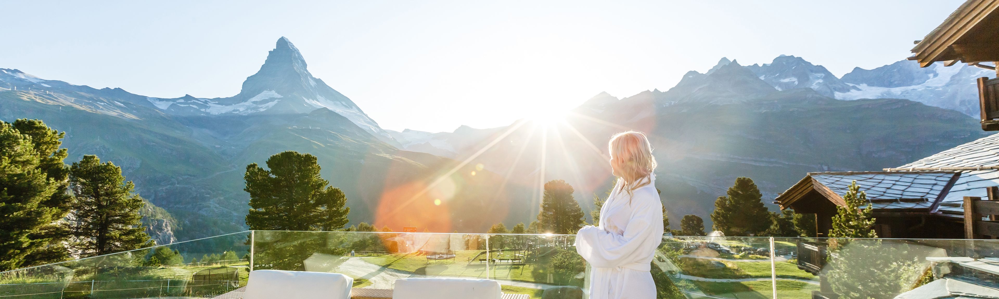Eine Frau steht auf der Dachterrasse eines Wellness Resorts und genießt den Blick auf das Bergpanorama
