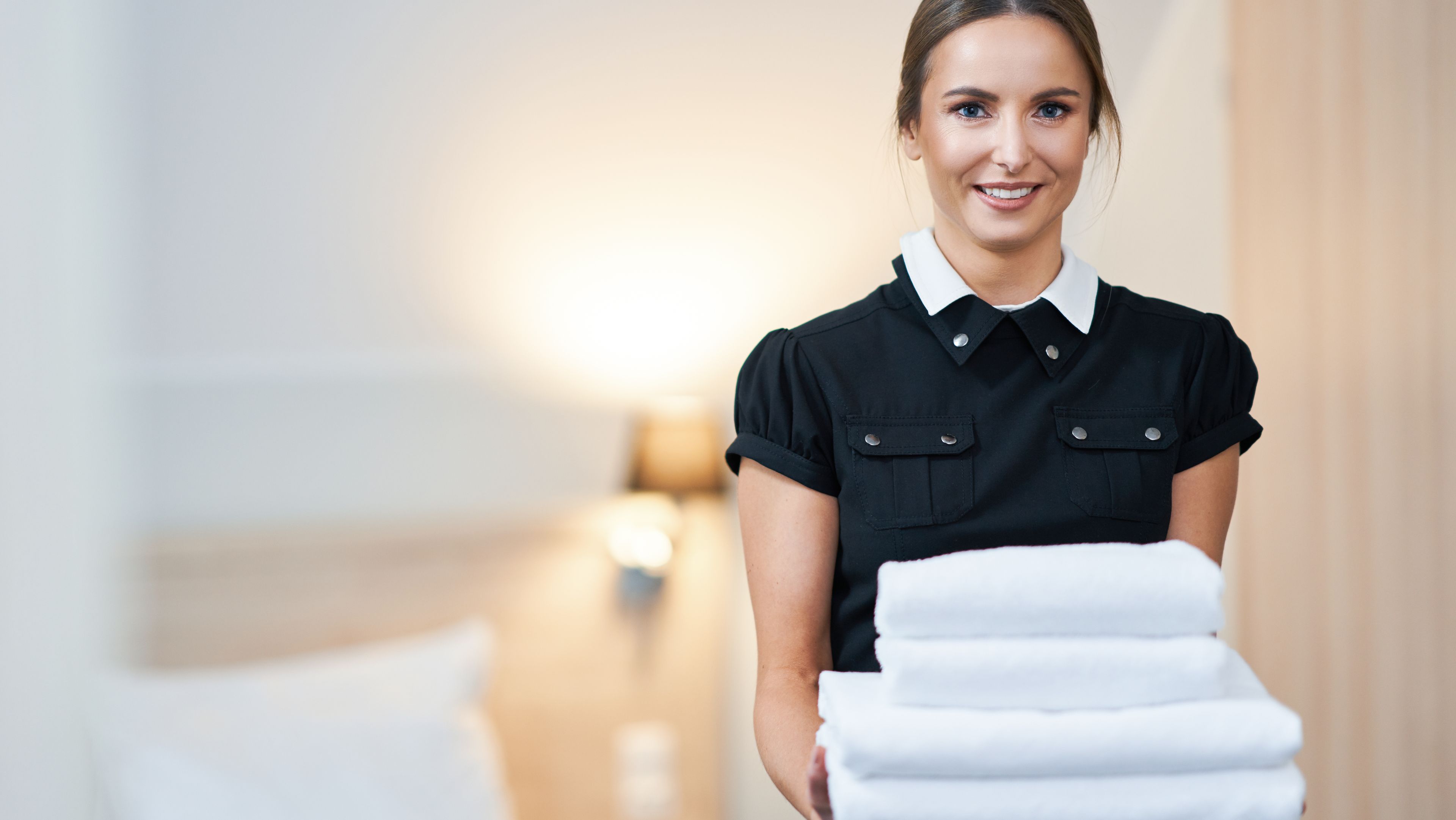 Eine Servicekraft hält einen Stapel mit Handtüchern im Hotelzimmer