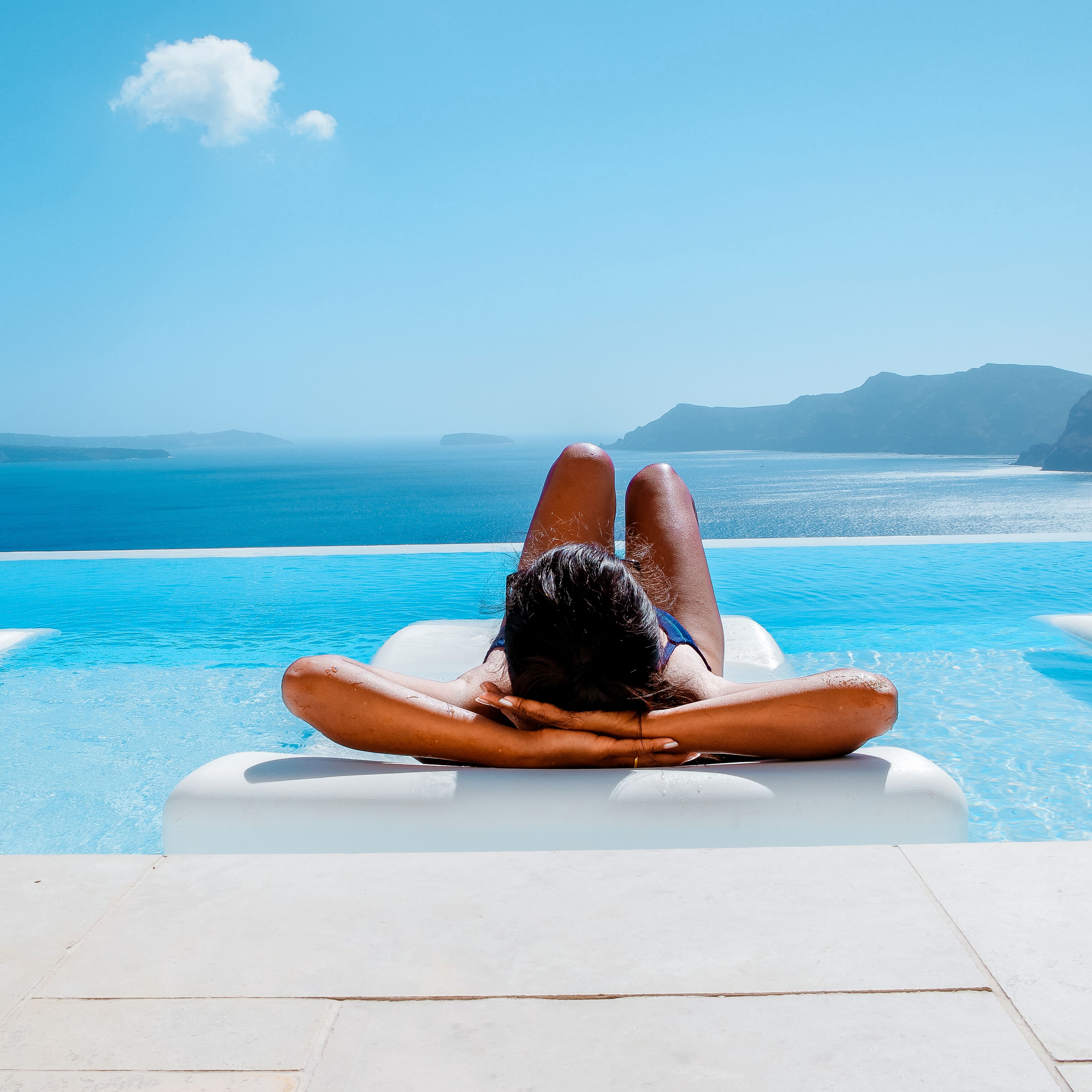 Frau liegt auf einer Luftmatratze im Pool und genießt den Blick auf das Meer