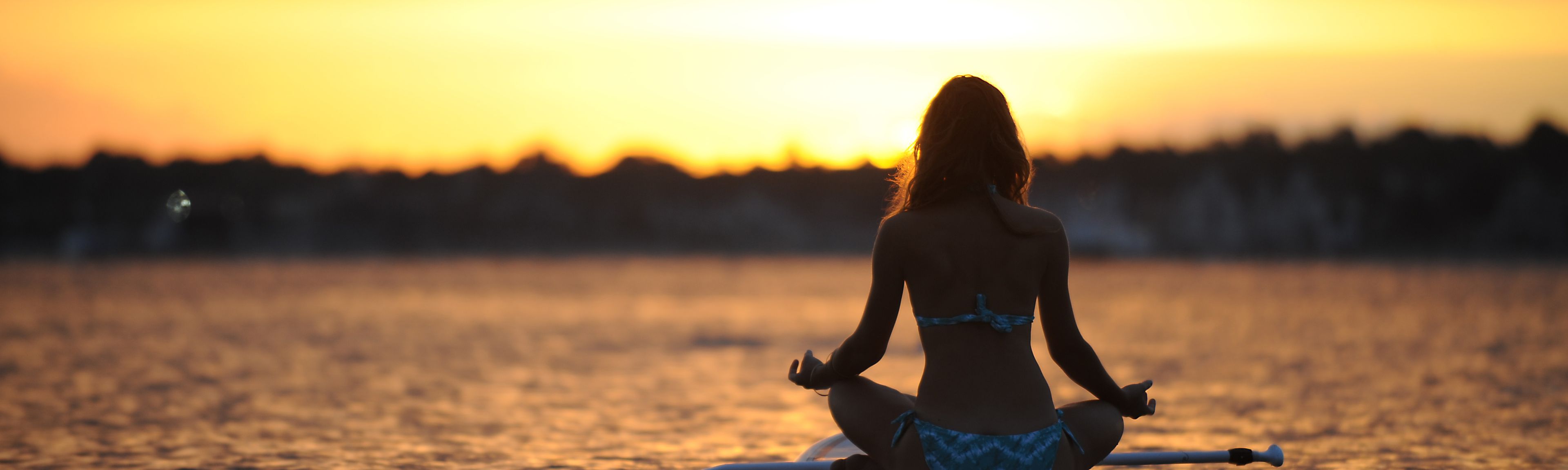 Frau auf dem Surfbrett sitzend auf dem See bei Sonnenuntergang