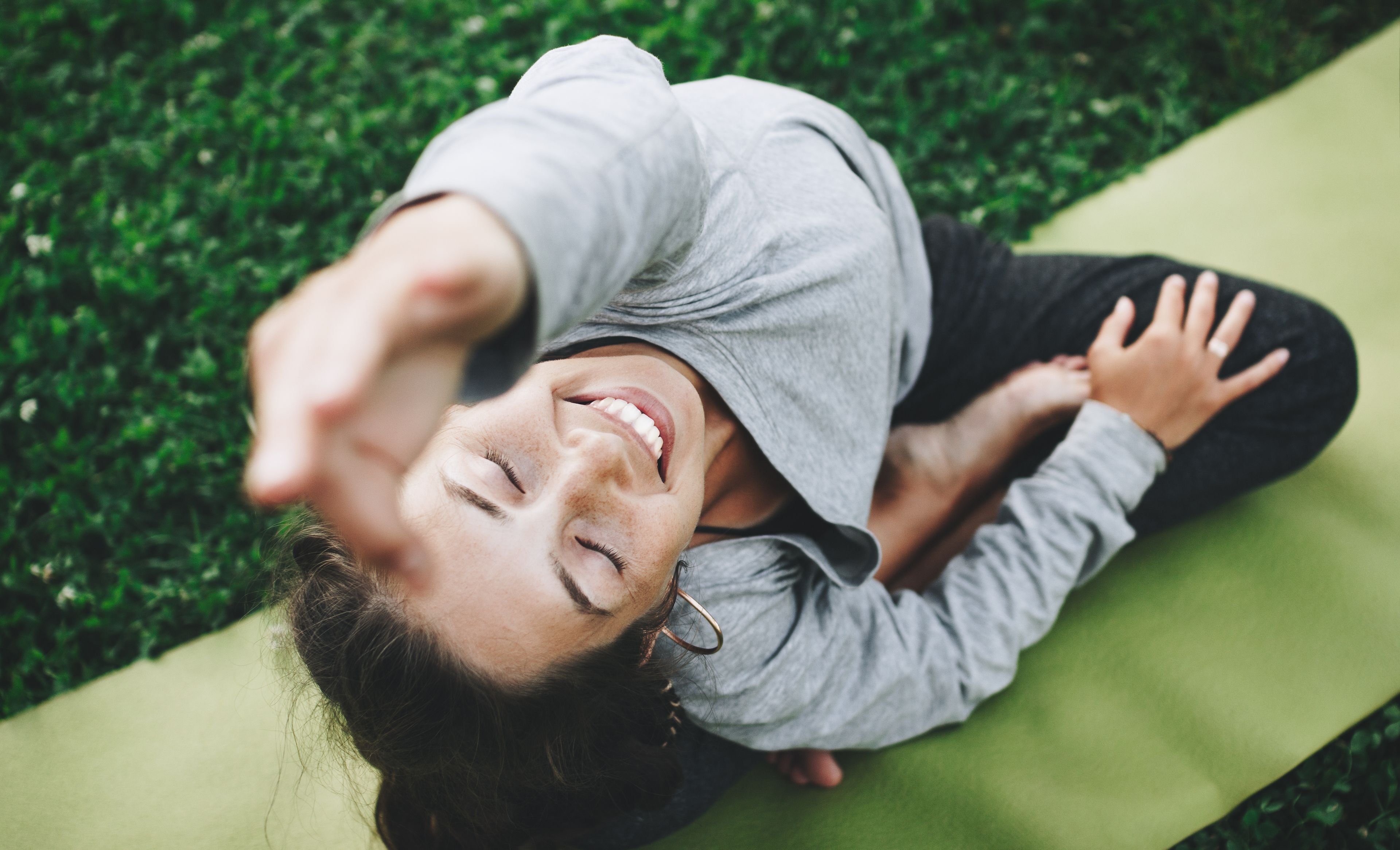 Frau auf Yogamatte sitzend, einen Arm in die Luft gestreckt, Blick nach oben