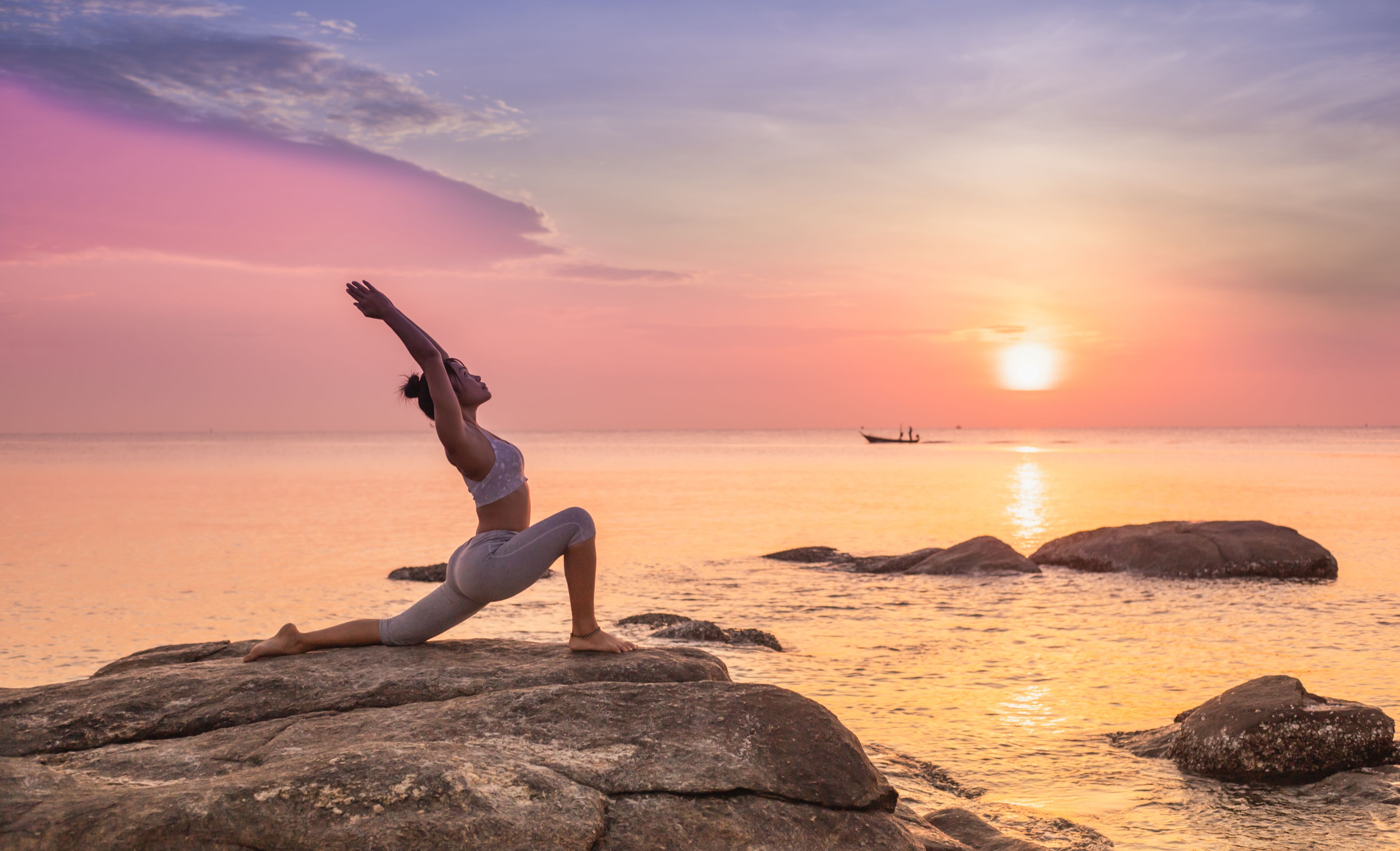Frau auf einem Felsen in Yogaposition bei Sonnenuntergang 