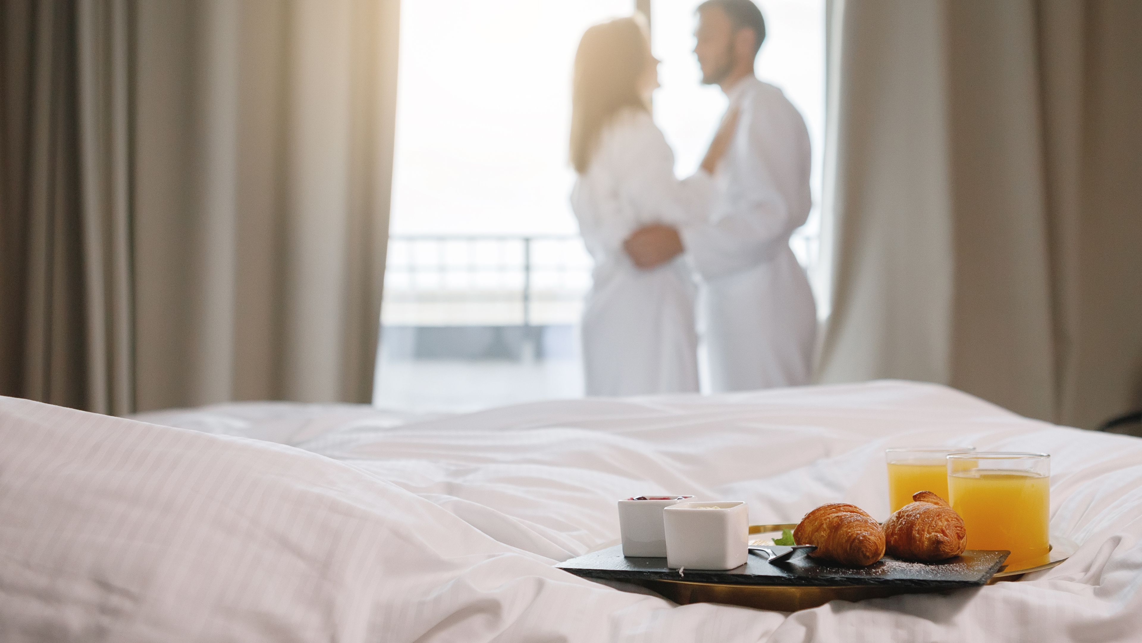 Pärchen im Hotelzimmer mit Frühstück auf dem Bett