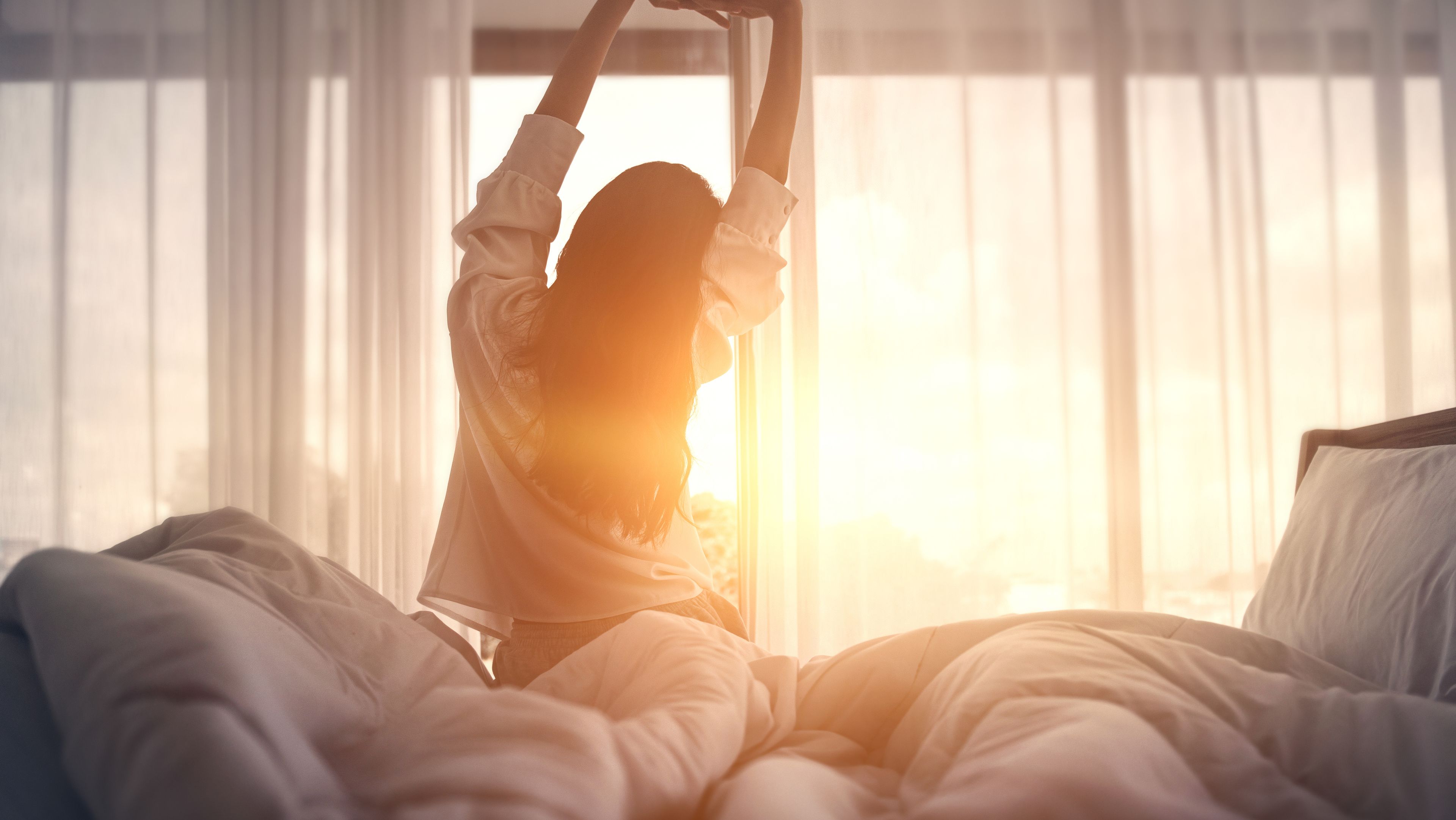 Une femme s'étire dans son lit à la lumière du soleil