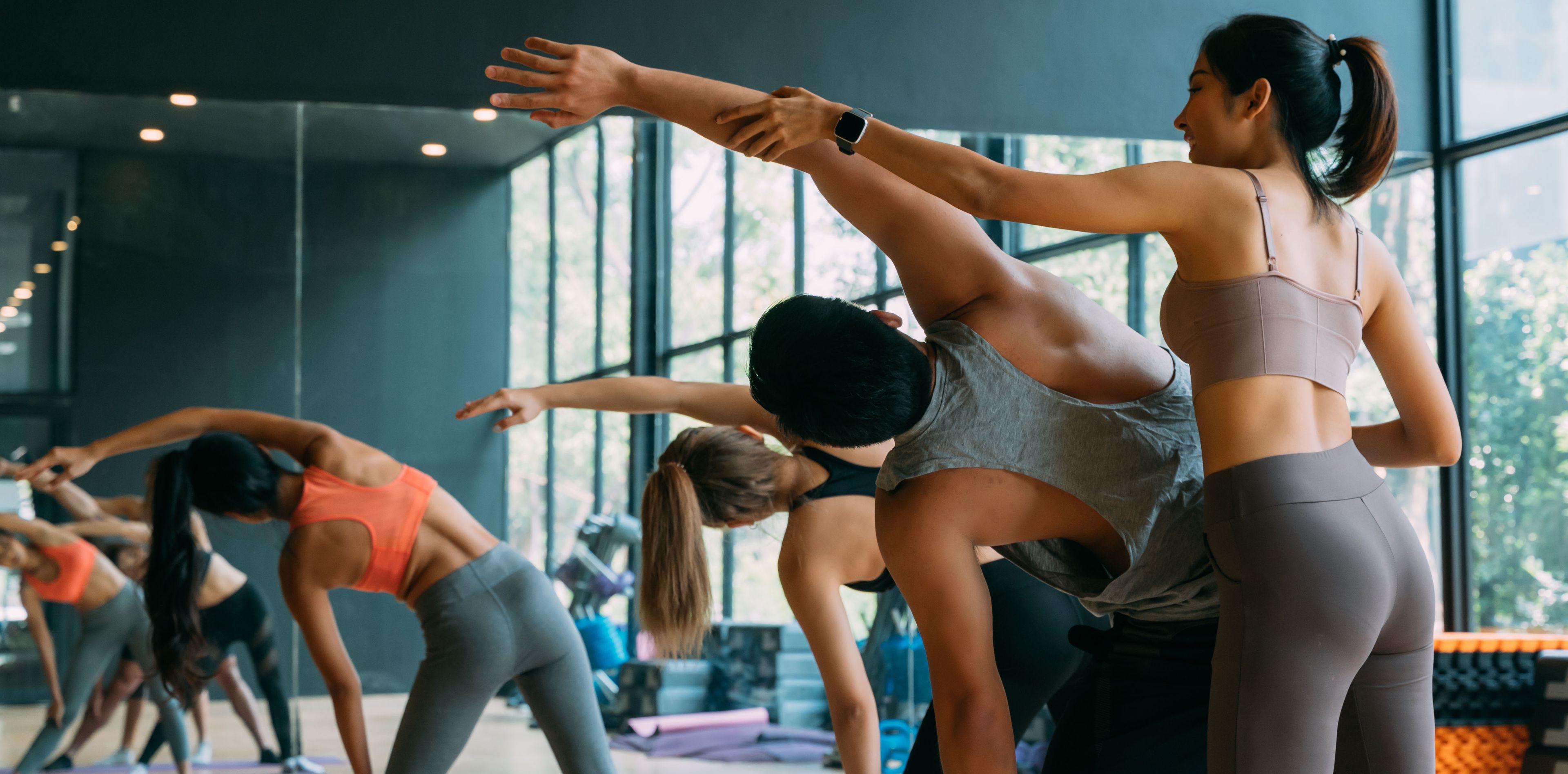 Mehrere Yogis in Yogastellung, eine Yoga Lehrerin korrigiert sie bei der Ausführung