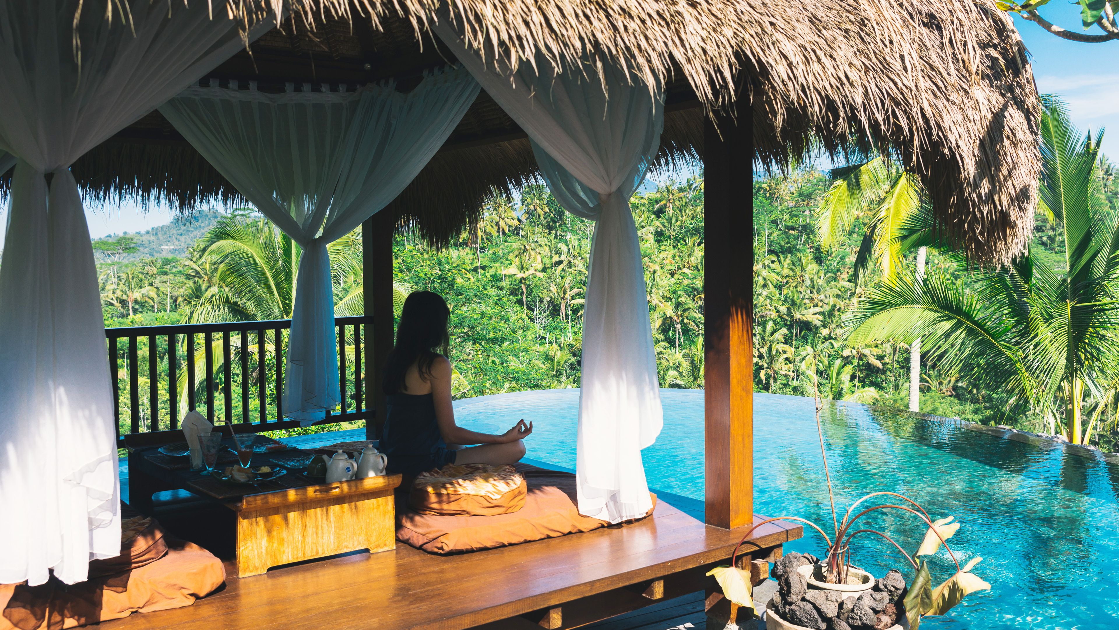 Ein Frau sitzt beim Yoga auf Bali und schaut auf den Hotelpool